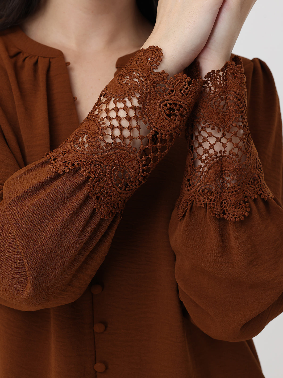 Brown blouse with lace detailing on sleeves against a neutral background