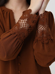 Brown blouse with lace detailing on sleeves against a neutral background