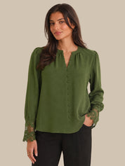 Woman wearing a green blouse with lace details on a beige background