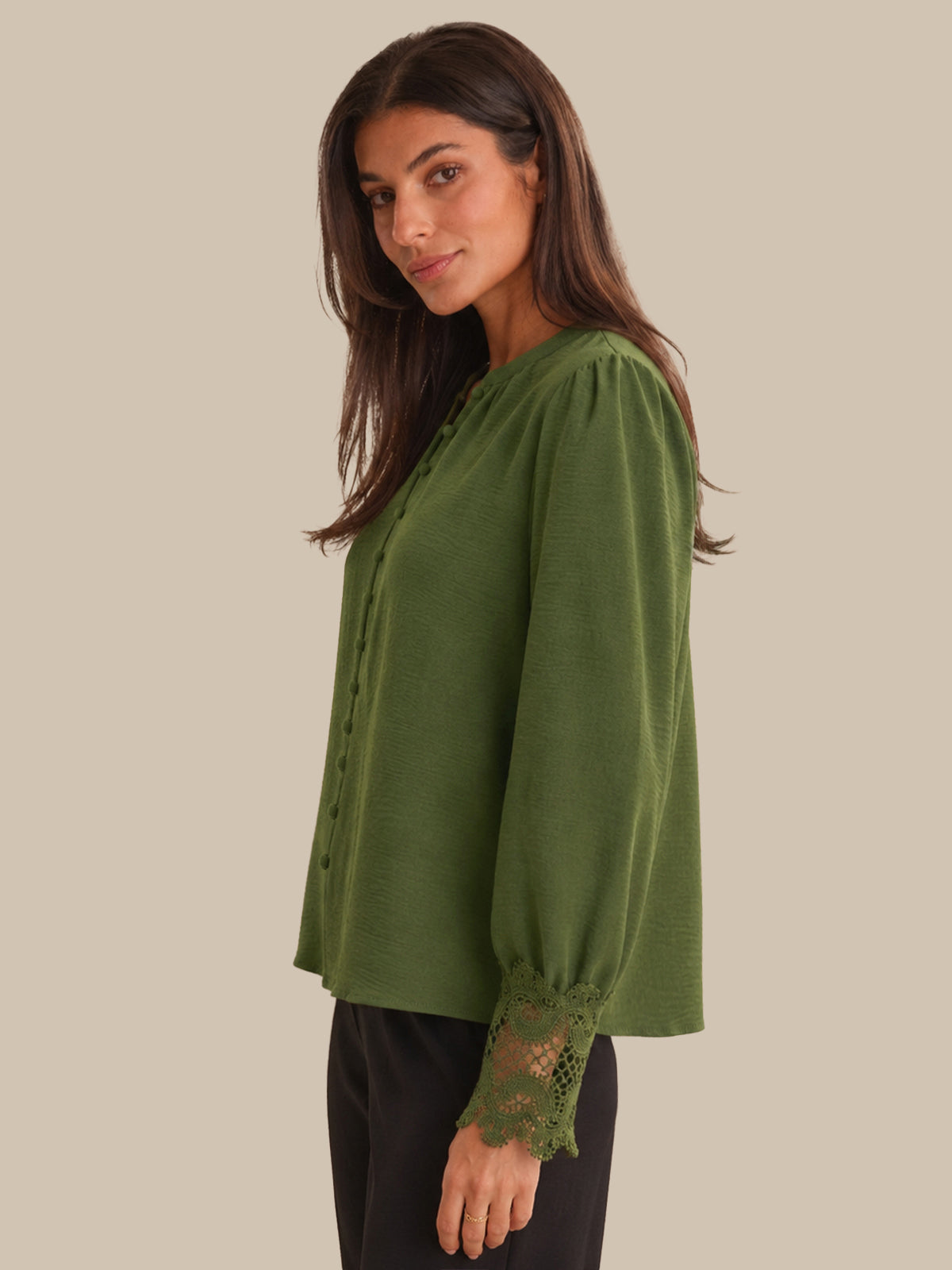 Woman wearing a green blouse with lace cuffs on a plain background