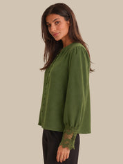 Woman wearing a green blouse with lace cuffs on a plain background