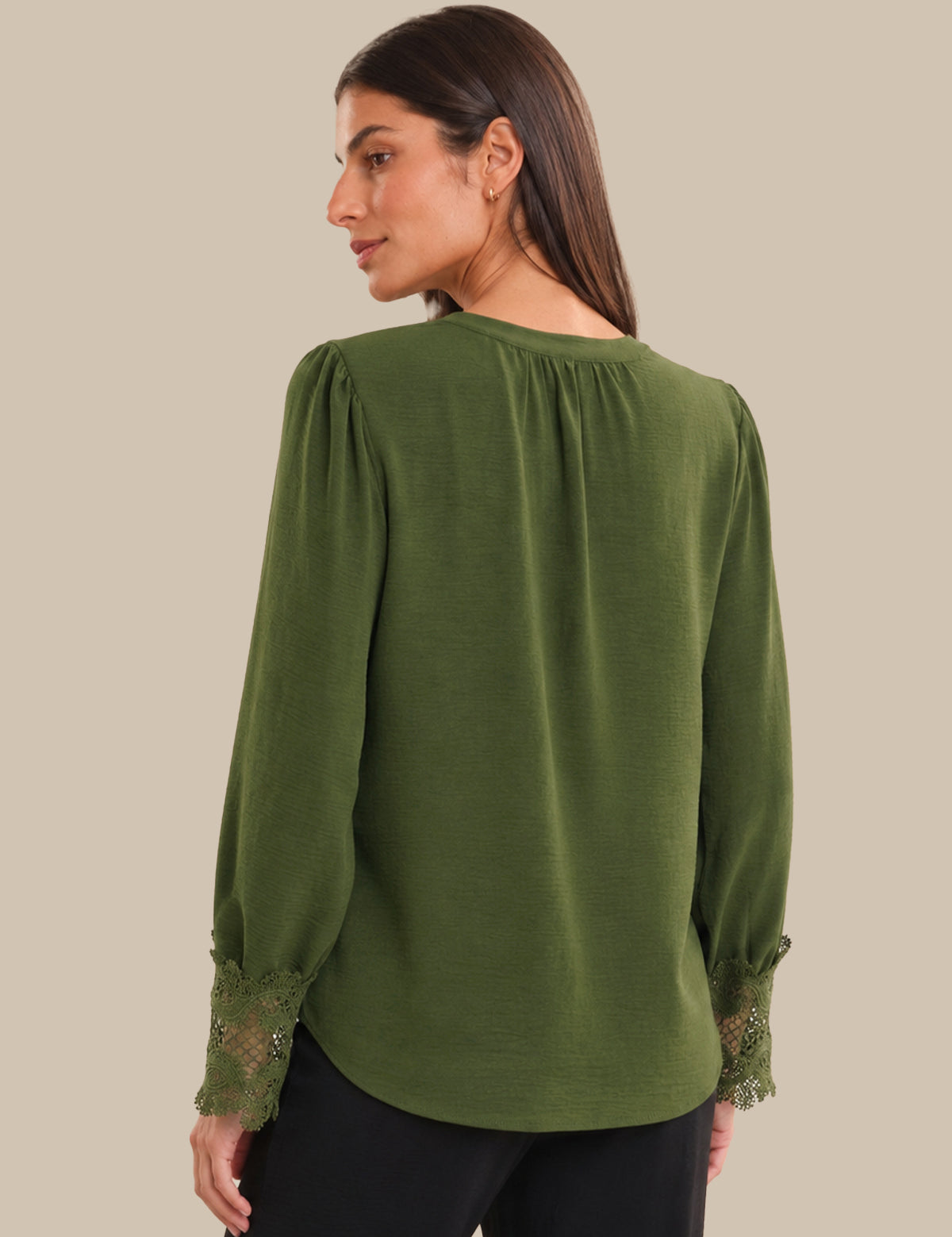 Woman wearing a green blouse with lace sleeves on a beige background
