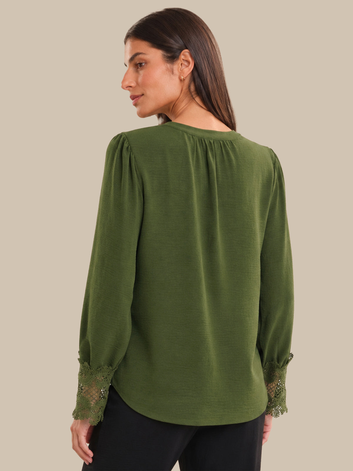 Woman wearing a green blouse with lace sleeves on a beige background