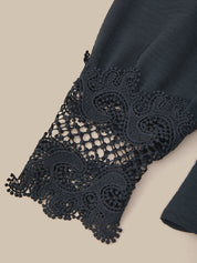 Close-up of a dark navy blue garment featuring an intricate, matching lace cuff with a scalloped and floral pattern, set against a solid beige background.