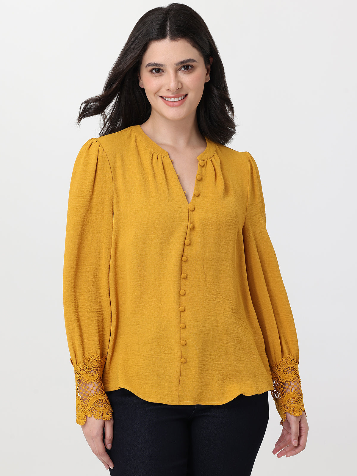 Woman wearing a mustard yellow blouse with lace cuffs on a white background