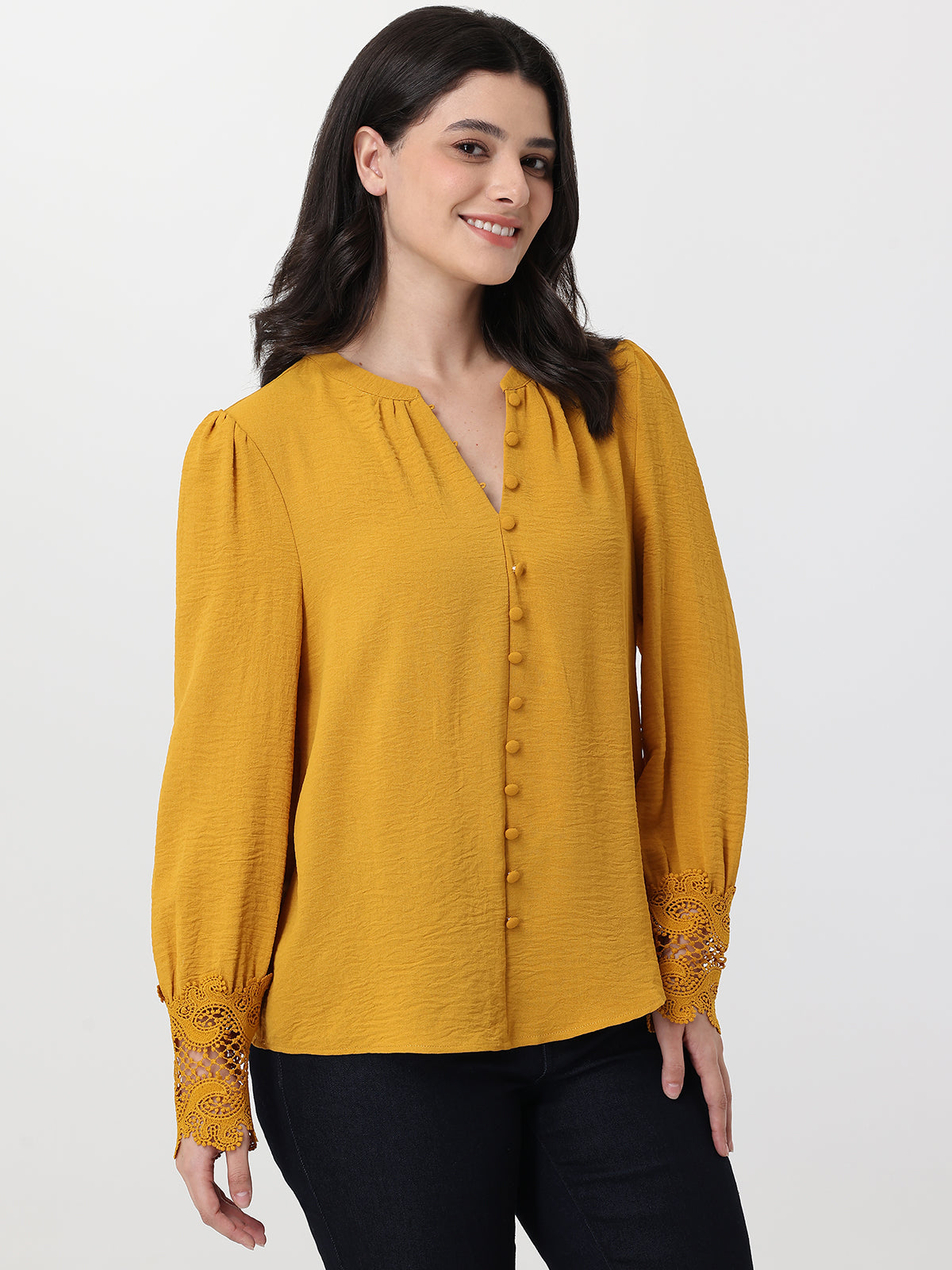 Woman wearing a mustard yellow blouse with lace details on a white background
