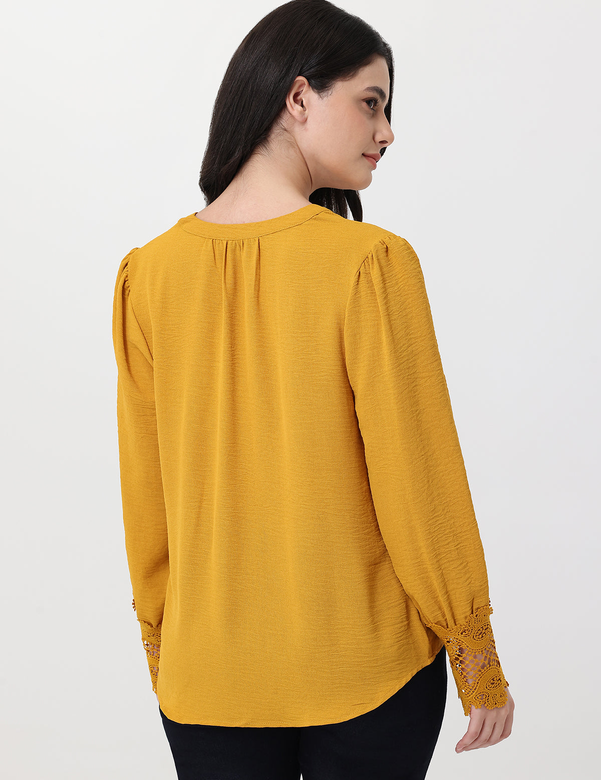 Woman wearing a mustard yellow blouse with lace cuffs on a white background