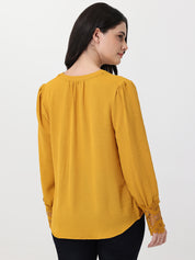 Woman wearing a mustard yellow blouse with lace cuffs on a white background