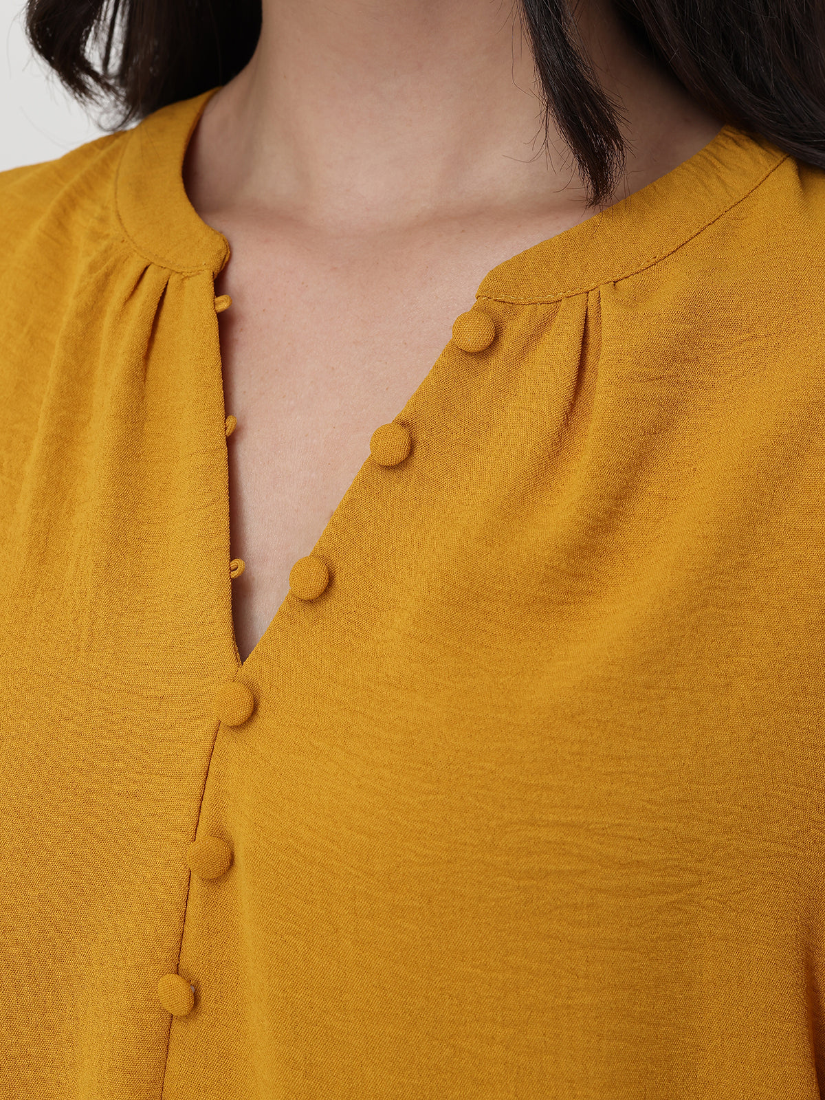 Close-up of a mustard yellow blouse with button details on a plain background