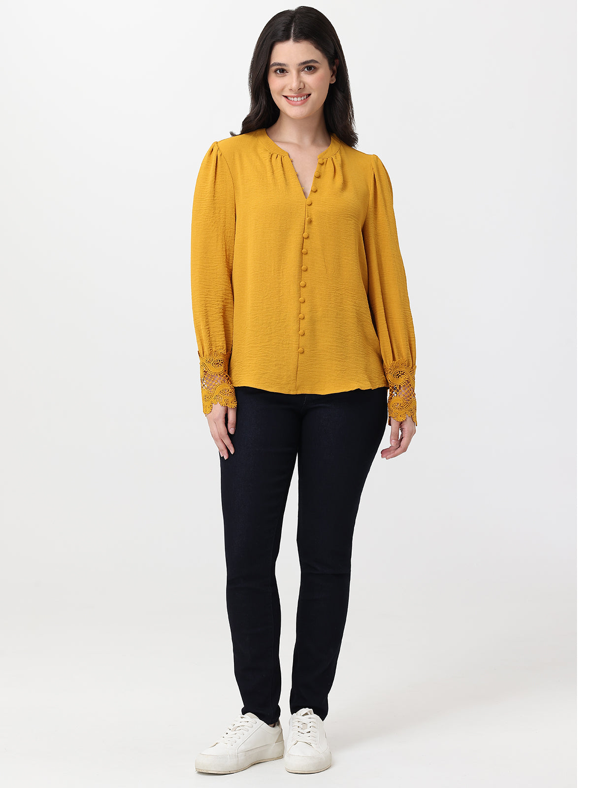 Woman wearing a mustard yellow blouse and black pants on a white background