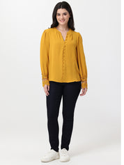 Woman wearing a mustard yellow blouse and black pants on a white background