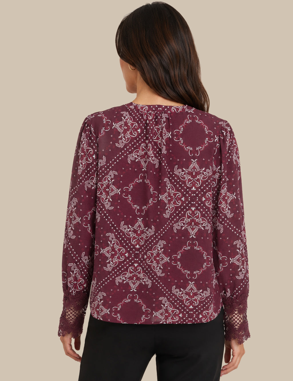 A woman shown from the back wearing a long-sleeve blouse with a burgundy and white paisley pattern, paired with black pants, against a solid beige background.