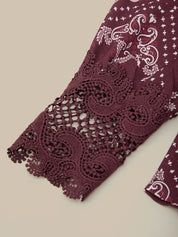 A close-up of a burgundy lace sleeve with white paisley and floral patterns, laid flat on a light beige background.