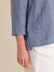 Close-up of a person wearing a blue striped shirt with a beige background