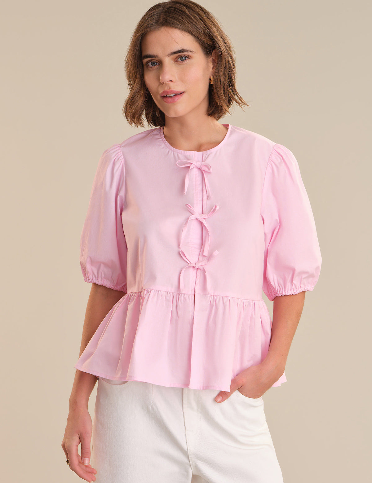 Woman wearing a pink blouse with puff sleeves against a beige background