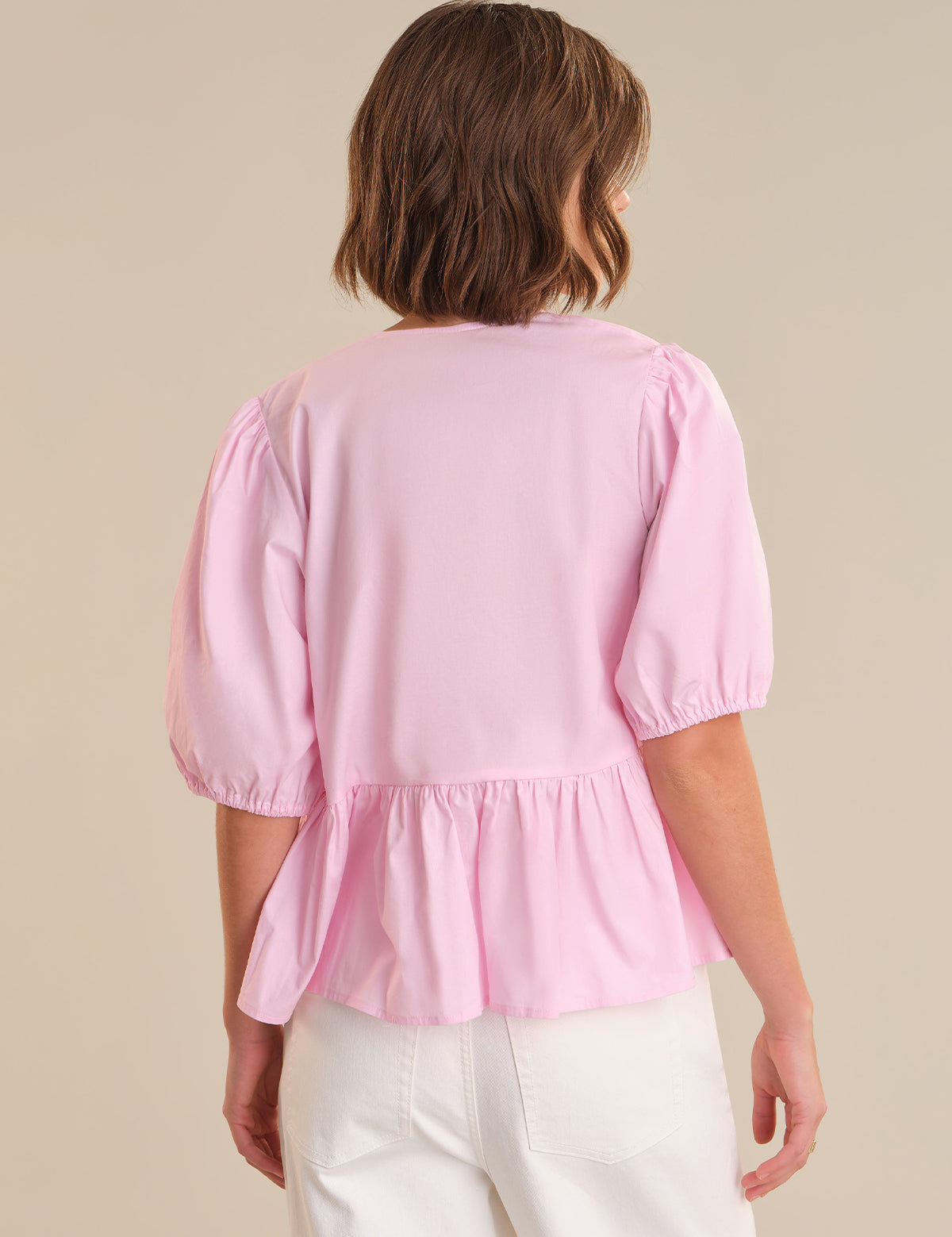 Person wearing a pink blouse with white pants on a beige background