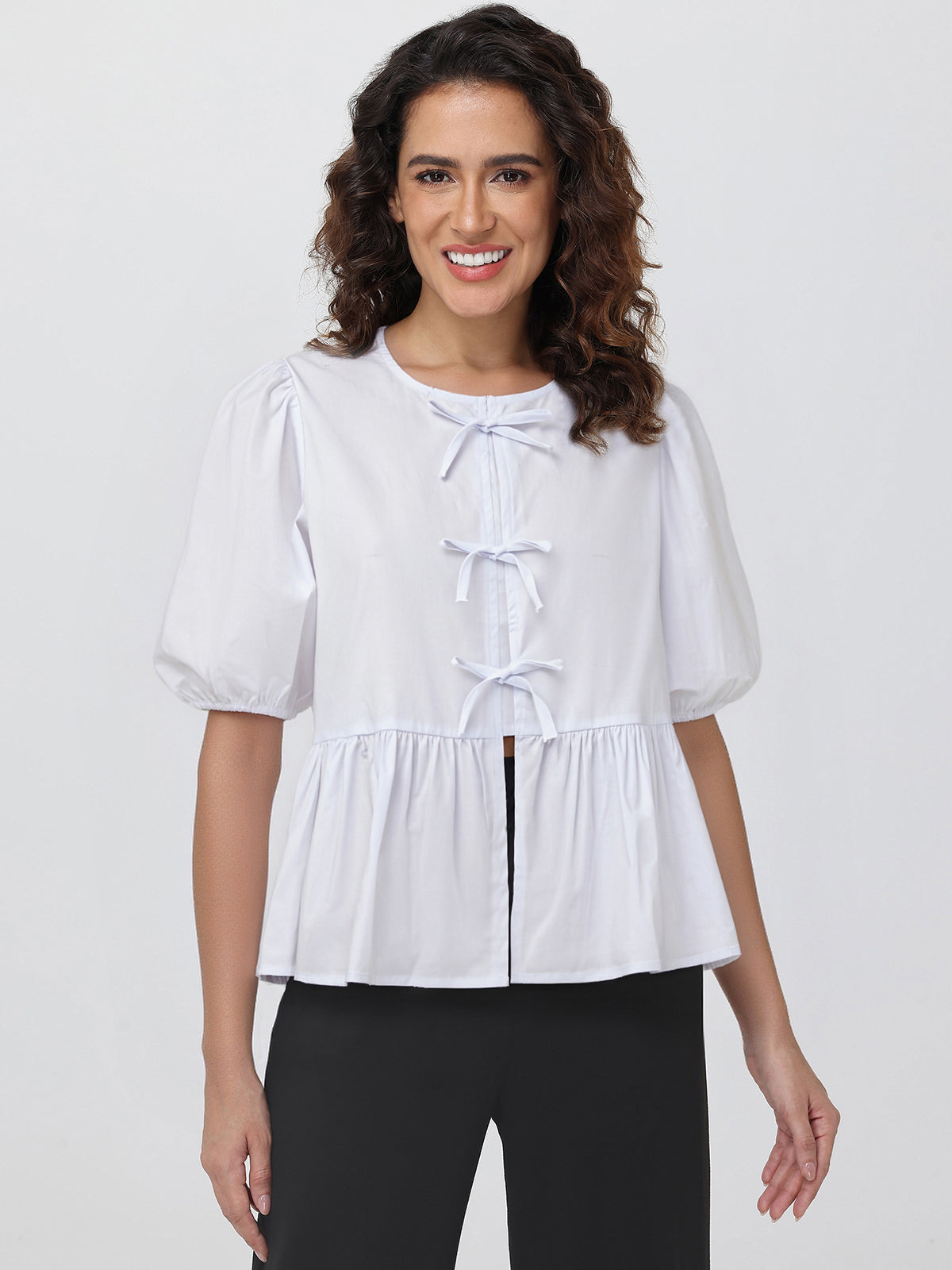 Woman wearing a white blouse with puff sleeves and a bow detail on a plain background