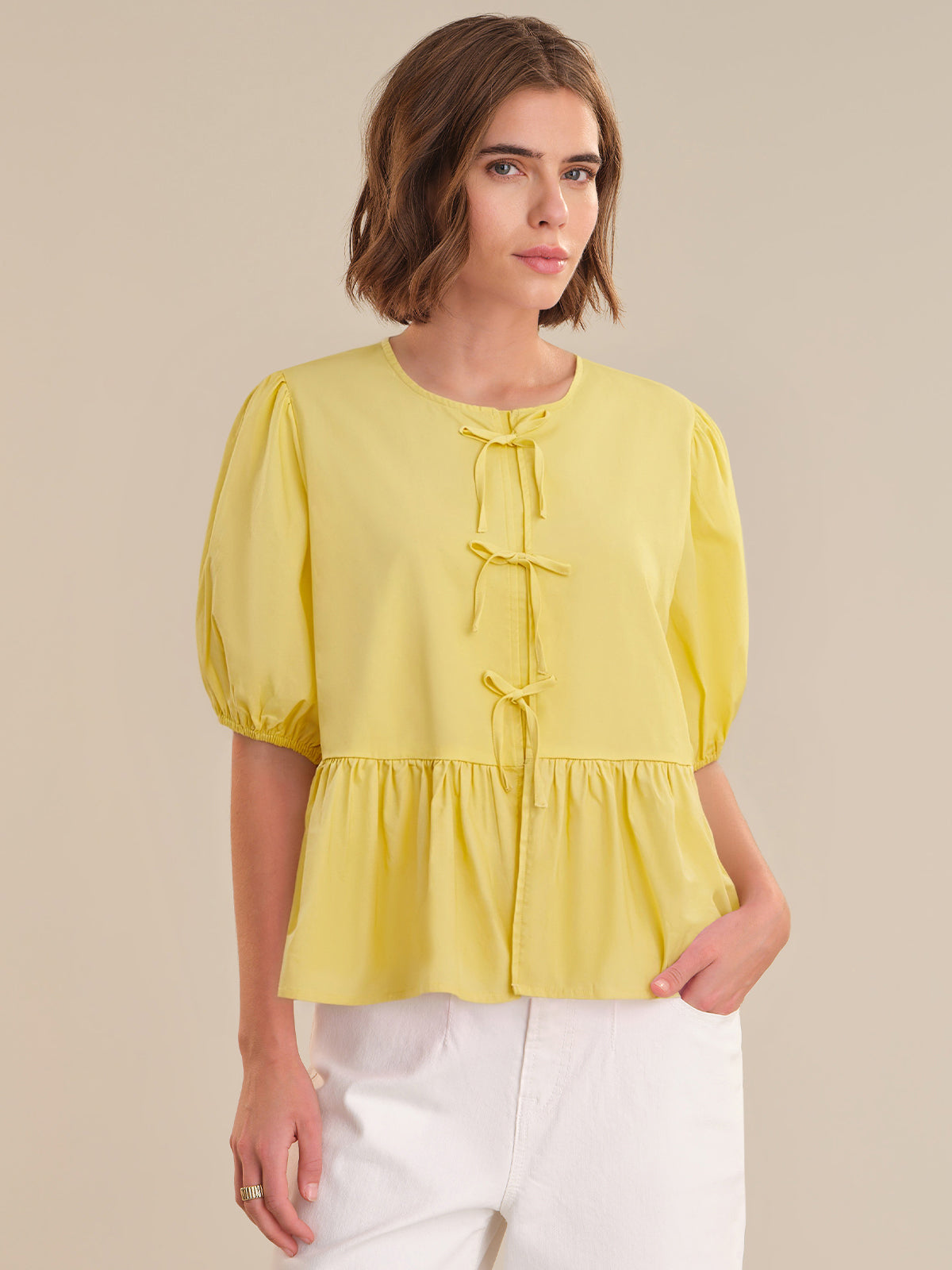 Woman wearing a yellow blouse with puff sleeves on a beige background