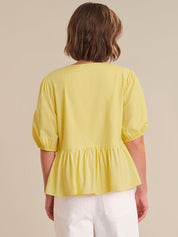 Person wearing a yellow blouse with white pants on a beige background