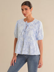 Woman wearing a light blue floral blouse with puffed sleeves against a beige background