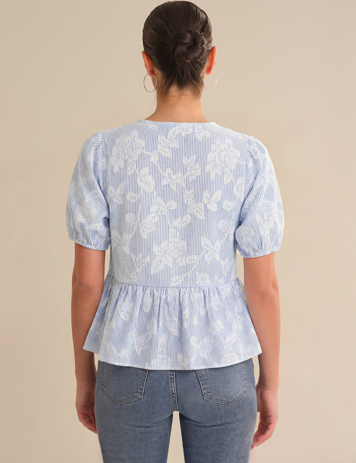 Person wearing a light blue floral peplum top and jeans on a beige background