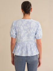 Person wearing a light blue floral peplum top and jeans on a beige background