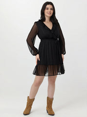 Woman wearing a black dress with sheer sleeves and hem, standing against a white background.