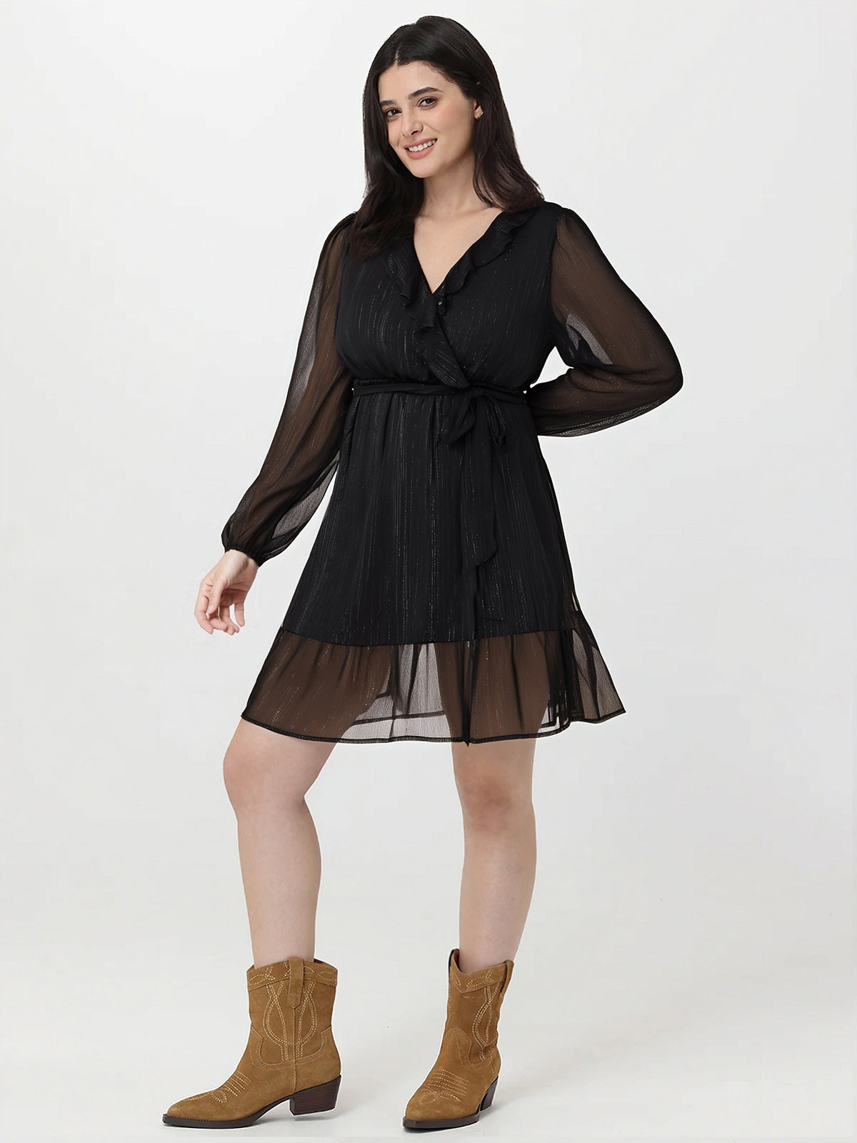 Woman wearing a black dress with sheer sleeves and hem, paired with brown boots on a white background