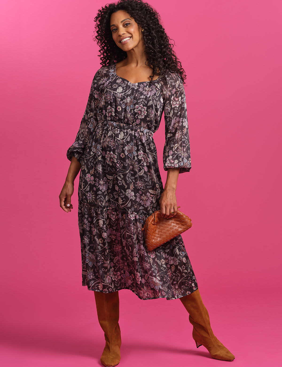 Woman wearing a floral dress and brown boots against a pink background
