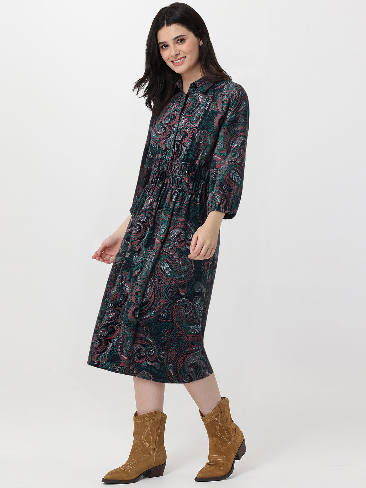 Woman wearing a patterned dress with long sleeves and brown boots on a white background