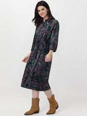 Woman wearing a patterned dress with long sleeves and brown boots on a white background