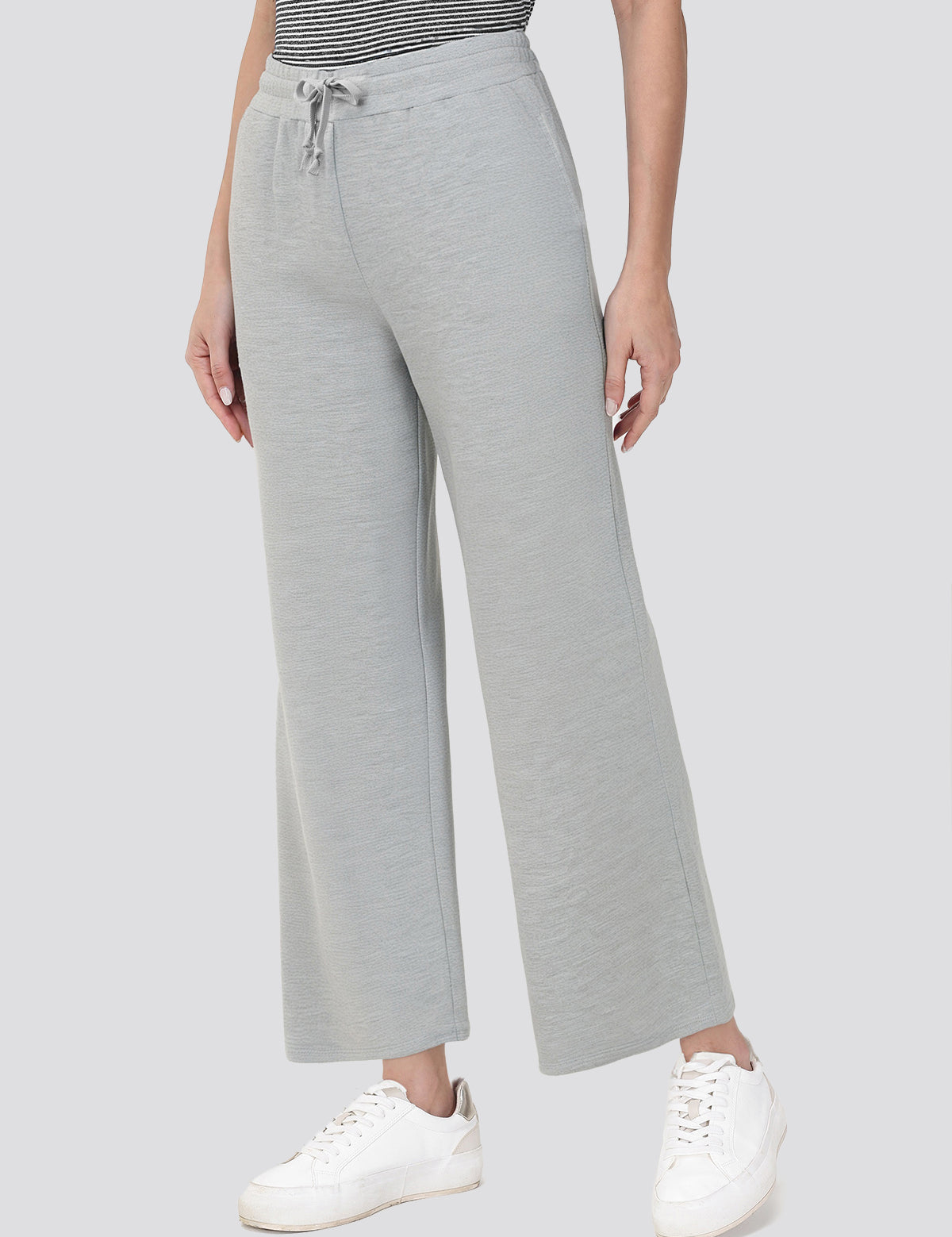 Person wearing gray wide-leg pants with a striped top and white sneakers on a light gray background