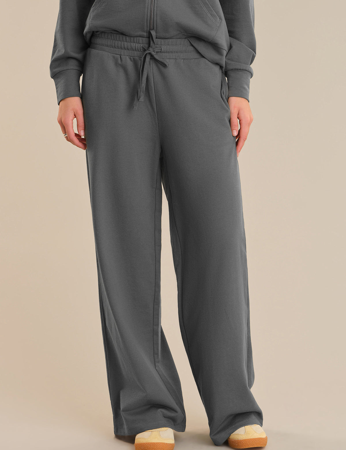 Person wearing gray sweatpants and a matching top on a beige background