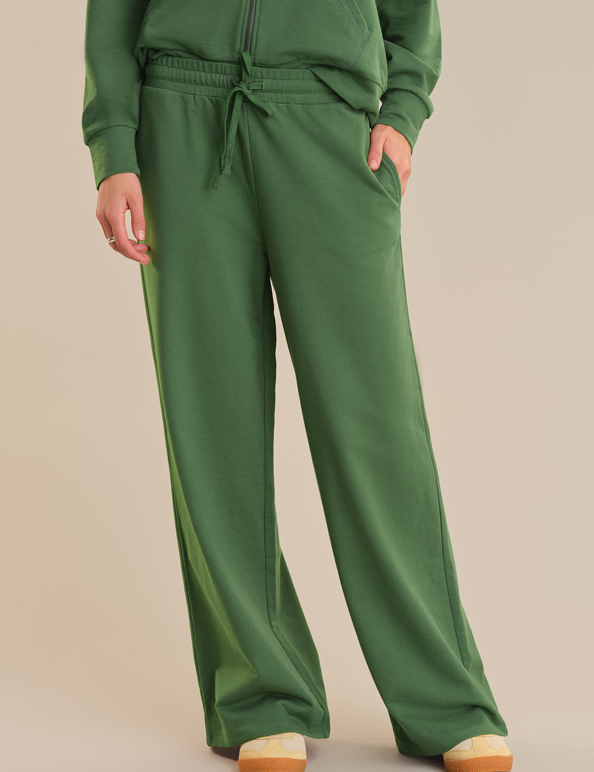 Green sweatshirt and pants worn by a person on a beige background