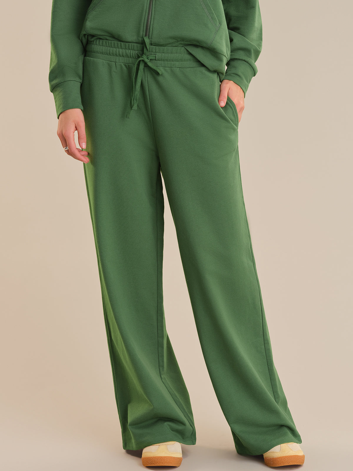 Green sweatshirt and pants worn by a person on a beige background