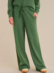 Green sweatshirt and pants worn by a person on a beige background