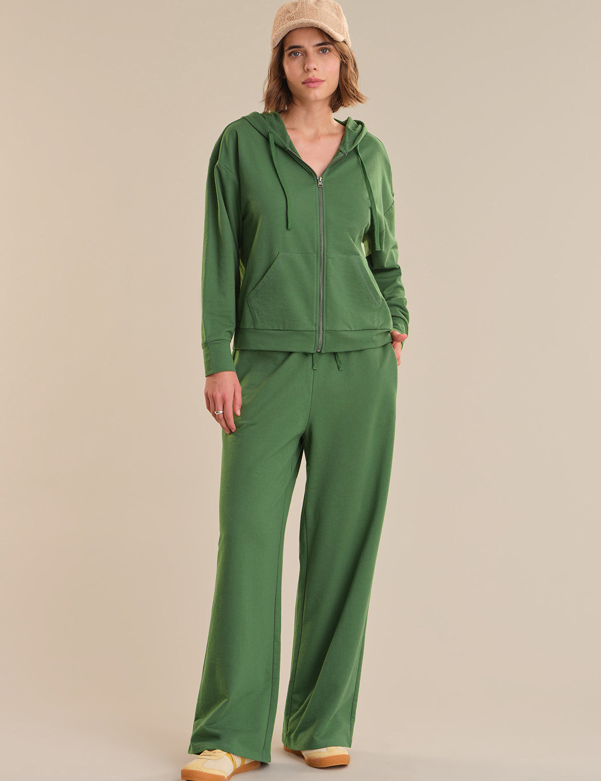 Person wearing a green tracksuit and beige cap on a beige background