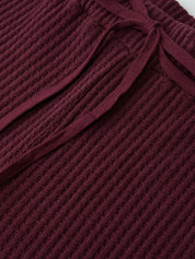 Close-up of a textured burgundy fabric with a bow detail.