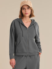 Woman wearing a gray zip-up hoodie and matching pants on a beige background