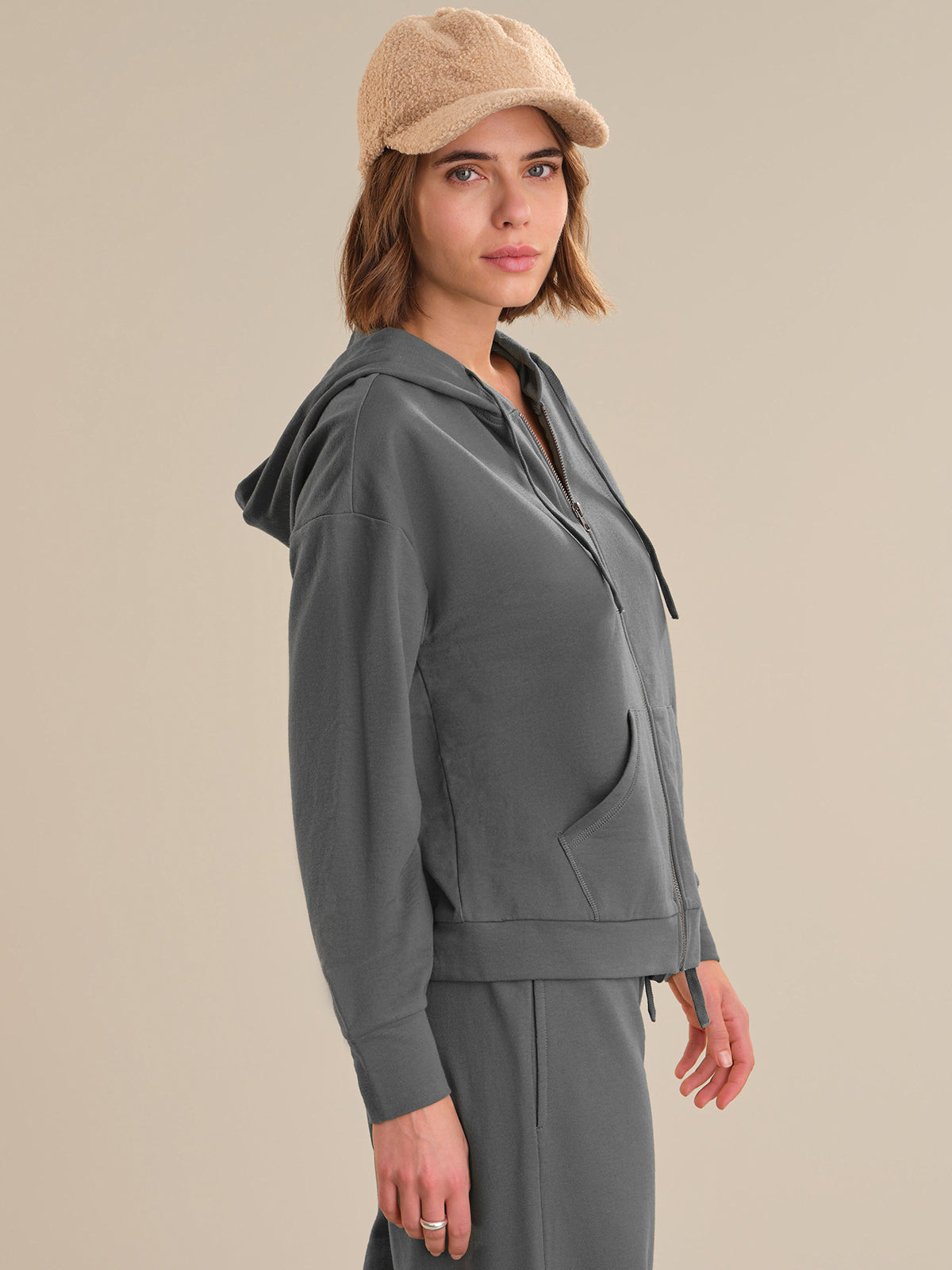 Woman wearing a gray hoodie and beige cap on a beige background