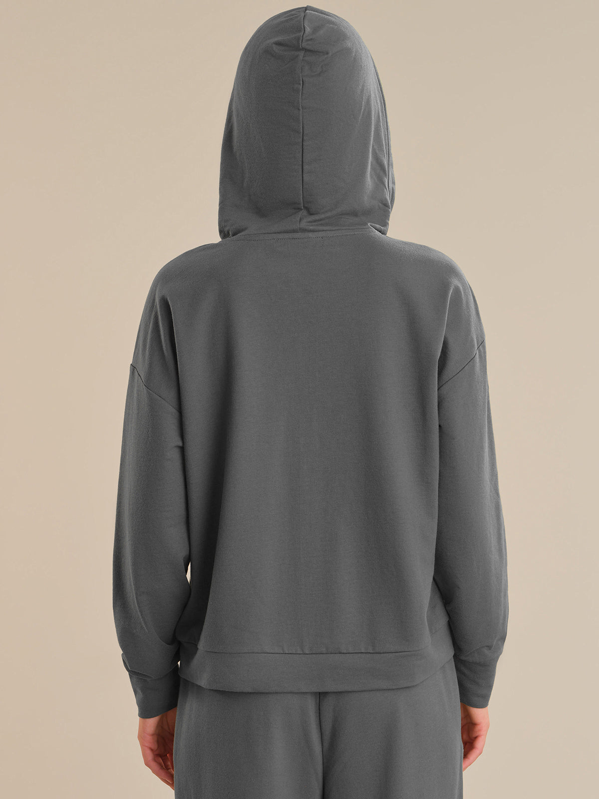 Person wearing a gray hoodie and pants on a beige background