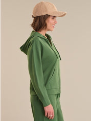 Woman wearing a green hoodie and matching pants with a beige cap on a beige background