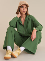Woman wearing a green tracksuit with beige shoes and cap on a neutral background