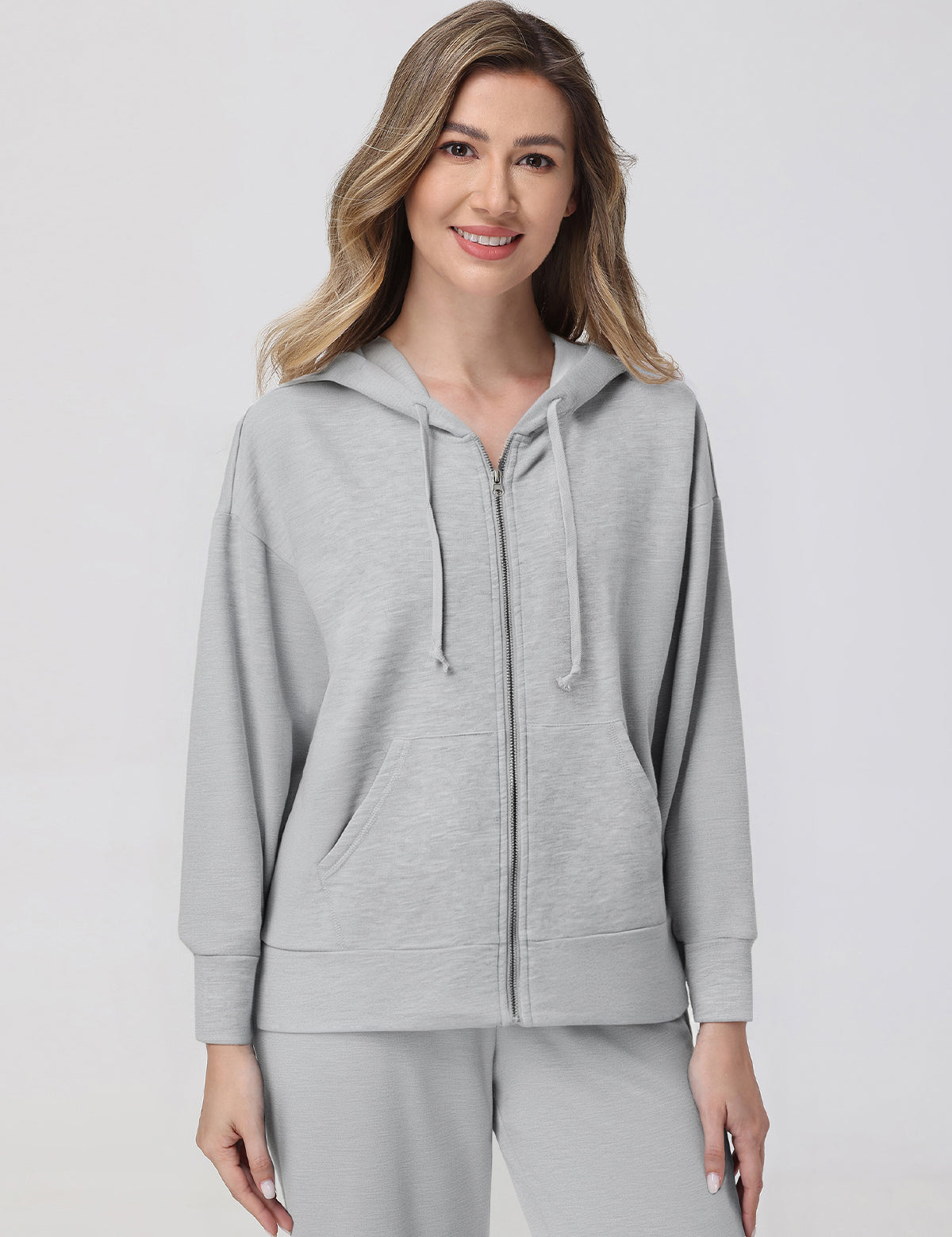 Woman wearing a gray hoodie and pants on a light gray background