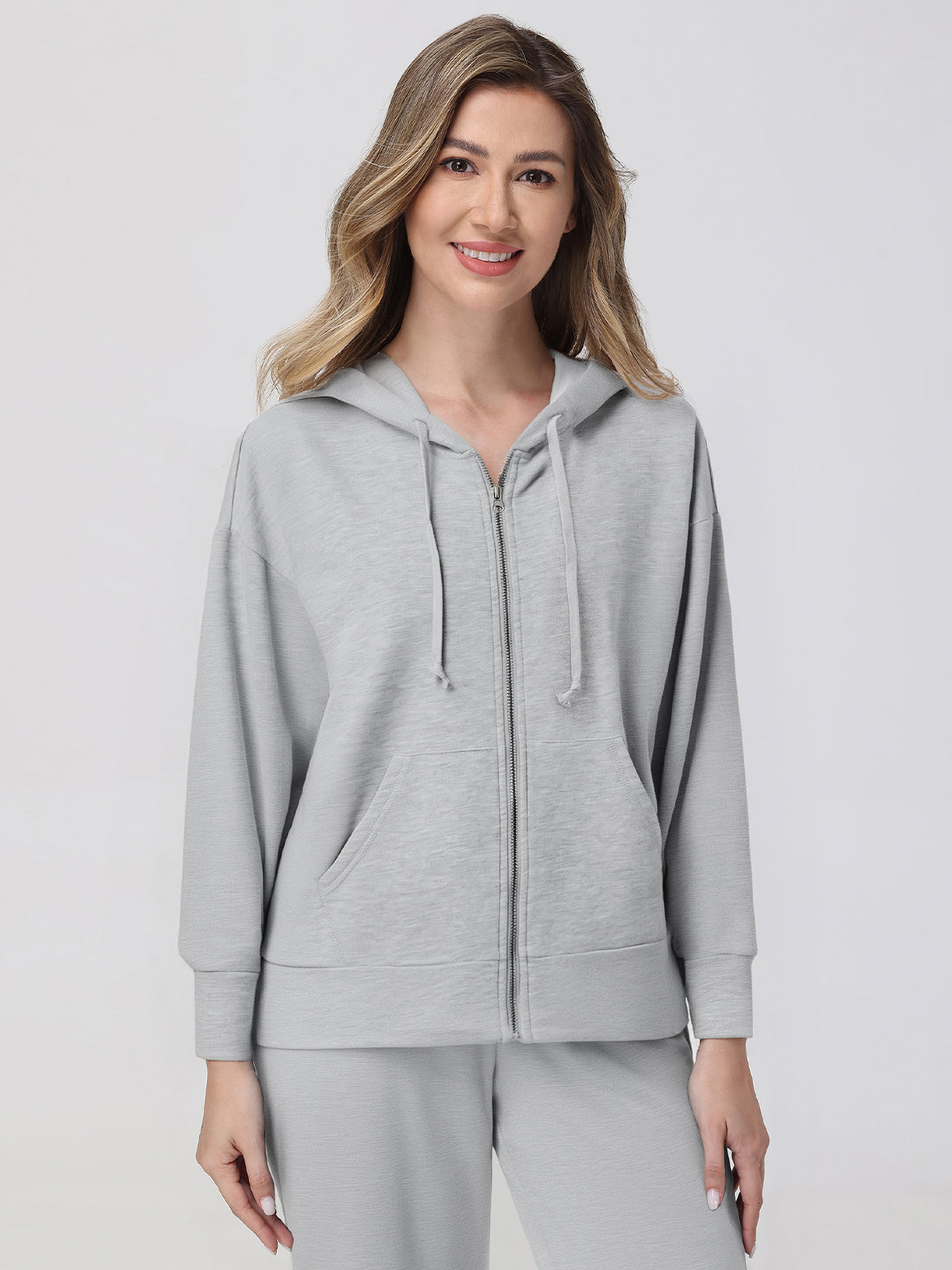 Woman wearing a gray hoodie and pants on a light gray background