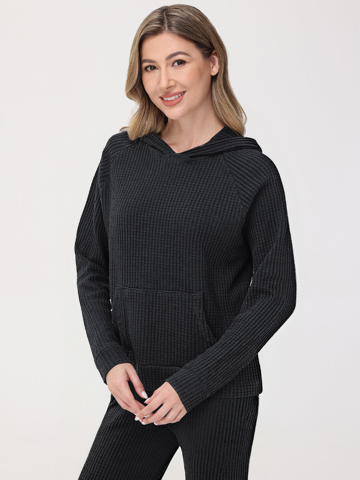 Woman wearing a black waffle knit hoodie and pants on a light gray background