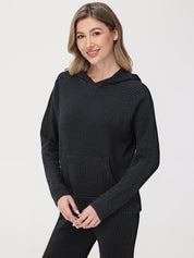 Woman wearing a black waffle knit hoodie and pants on a light gray background