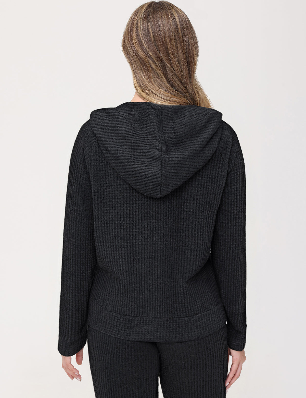 Person wearing a black textured hoodie and pants on a white background