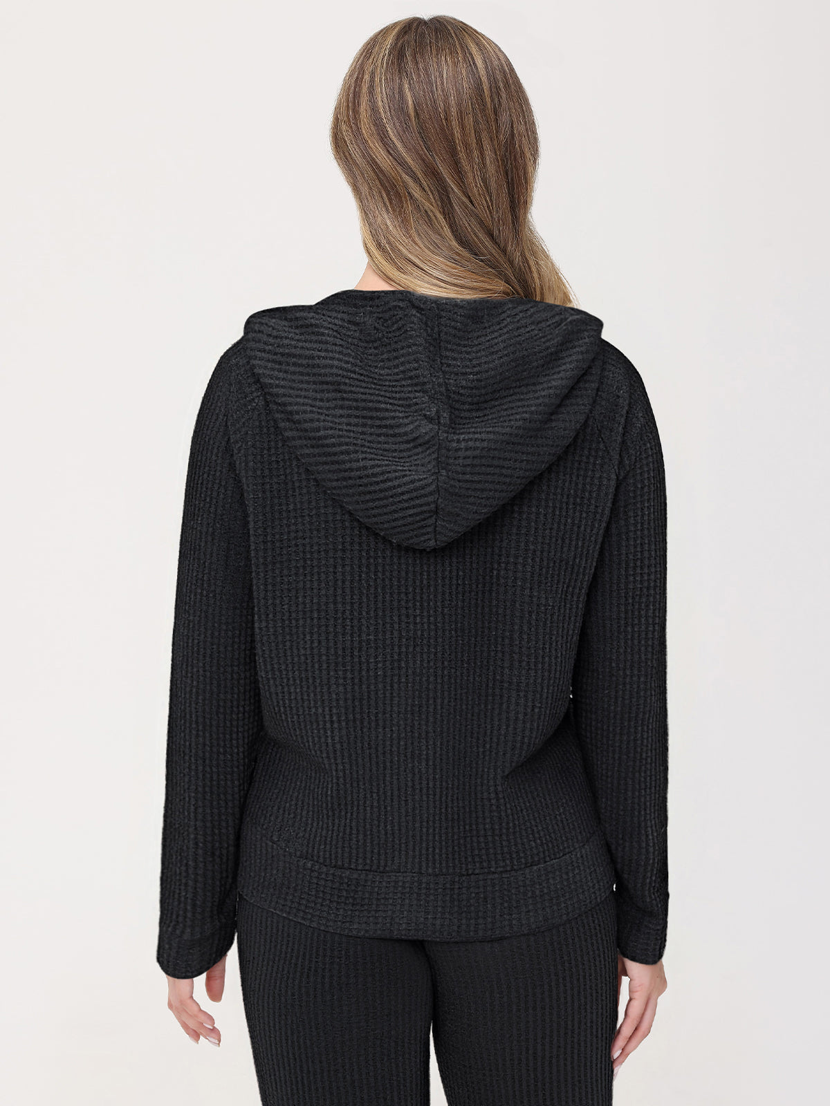 Person wearing a black textured hoodie and pants on a white background