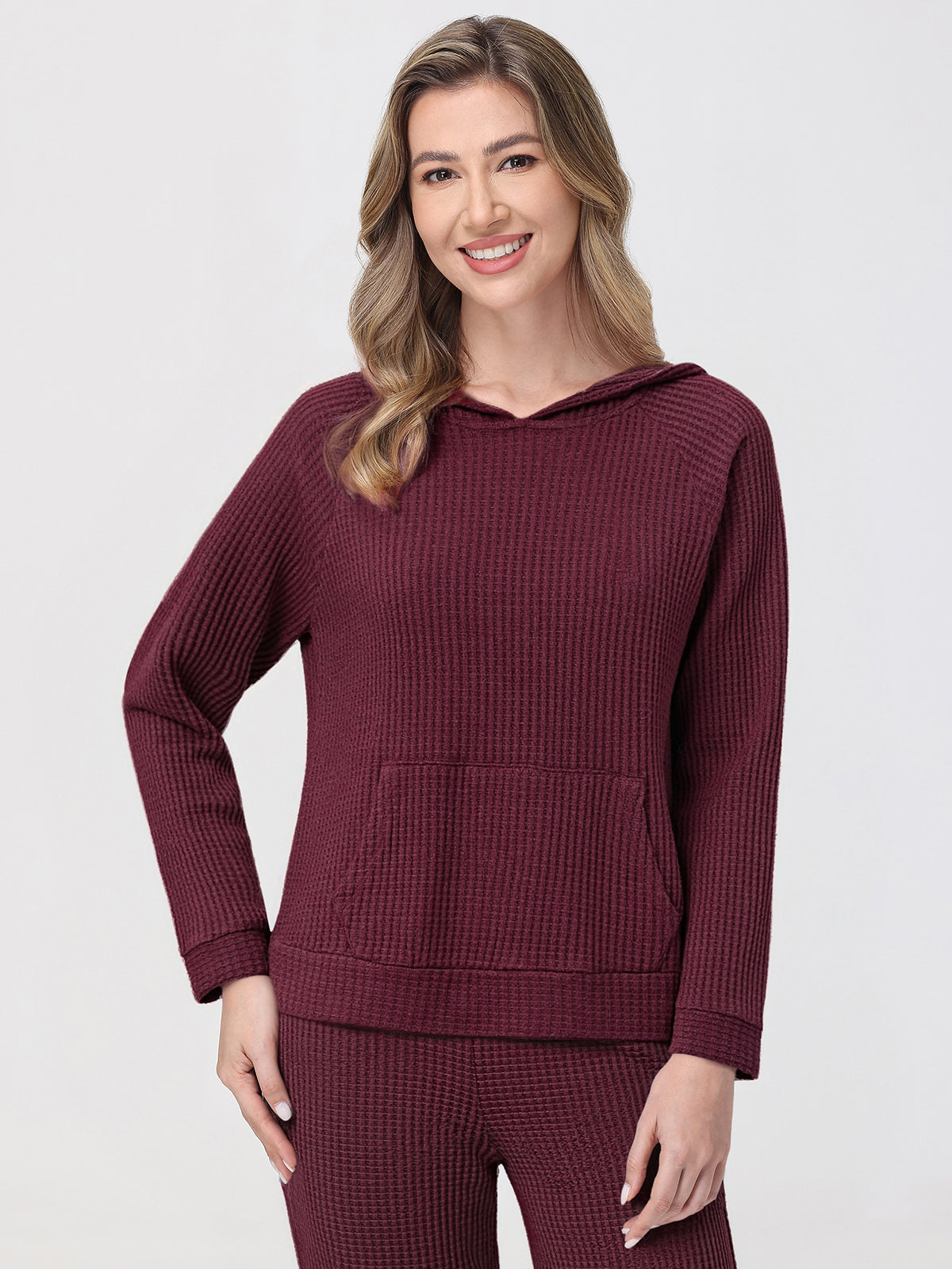 Woman wearing a burgundy waffle-textured hoodie and pants on a light gray background